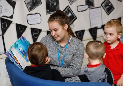 Early years worker reading book to pupils